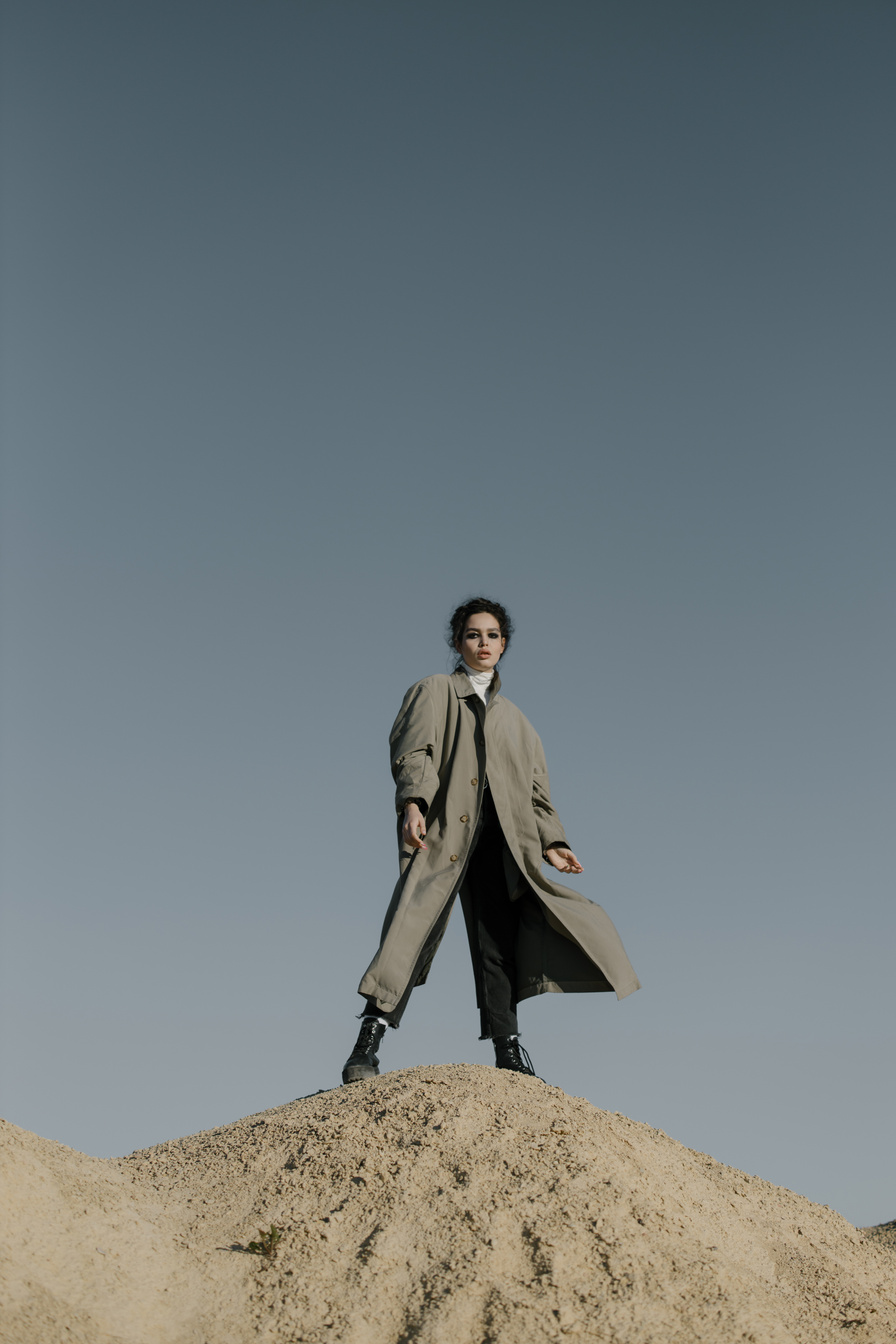 Man in Brown Coat Standing on Rock Under Blue Sky